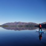 Glass calm water on Derwentwater with paddleboarder touring the lake