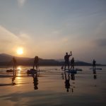 Stand Up Paddleboarders paddling on a very flat lake at sunset with views of Grisedale pike in the background