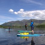 paddleboarders with instructor paddling across Derwent water with Skiddaw and Keswick in the back ground
