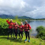 Four people dressed in wetsuits and spray jackets about to go paddleboarding on Derwentwater