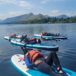 Paddle boards lying on board relaxing on Derwentwater with cat bells mountain in the background.